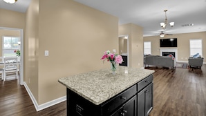 A spacious kitchen with a granite countertop, a dining area with a white table and chairs, and a living room with a fireplace and seating. - Spacious Family Retreat Near Camp Lejeune, Swansboro & Hammocks Beach (Hubert)