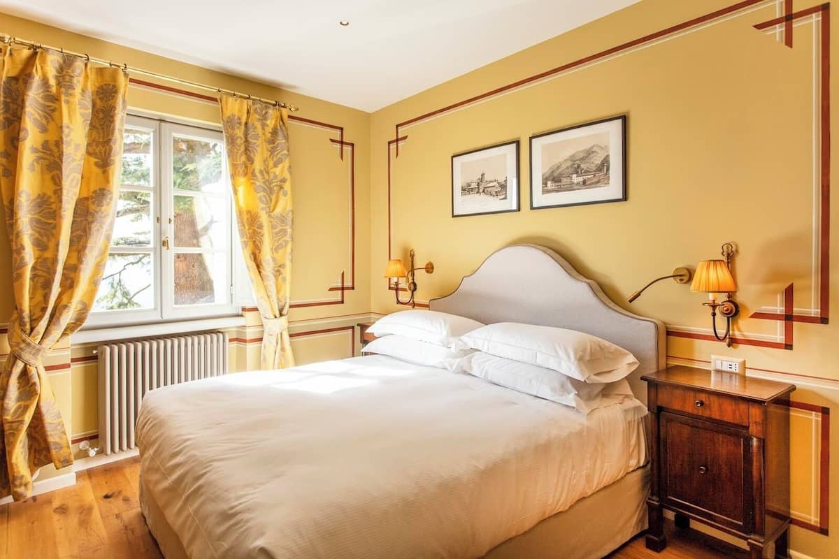 A bedroom with a large bed, two bedside lamps, a radiator, and two framed pictures on the wall.