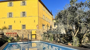 A yellow building with a stone wall and a swimming pool reflecting the building and trees. - Palazzo Tiglio - A Small Luxury Hotels of the World (Bucine)