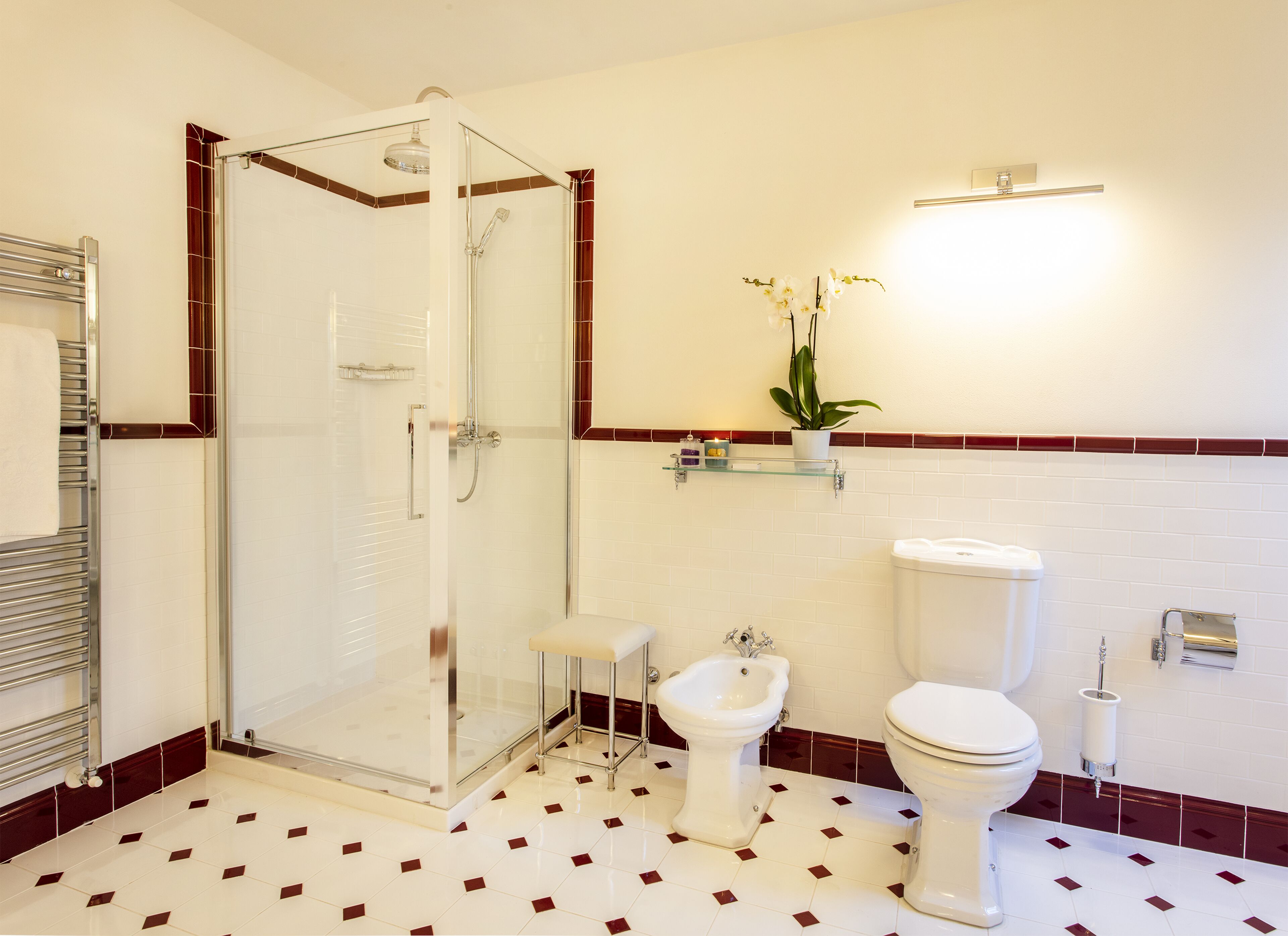 A bathroom with a glass-enclosed shower, a bidet, a toilet, and a shelf with a potted plant.