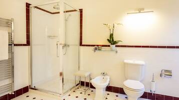 A bathroom with a glass-enclosed shower, a bidet, a toilet, and a shelf with a potted plant.