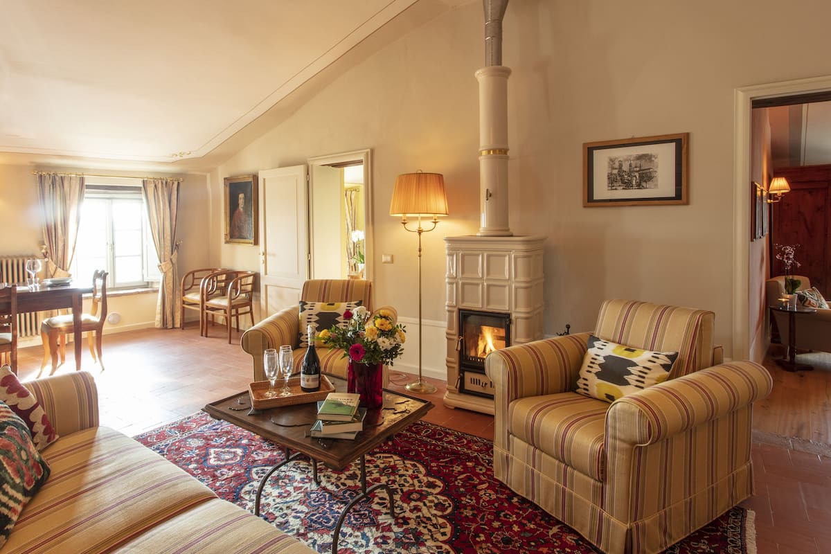 A cozy living room with a fireplace, striped sofas, a dining area with a table and chairs, and a patterned rug.