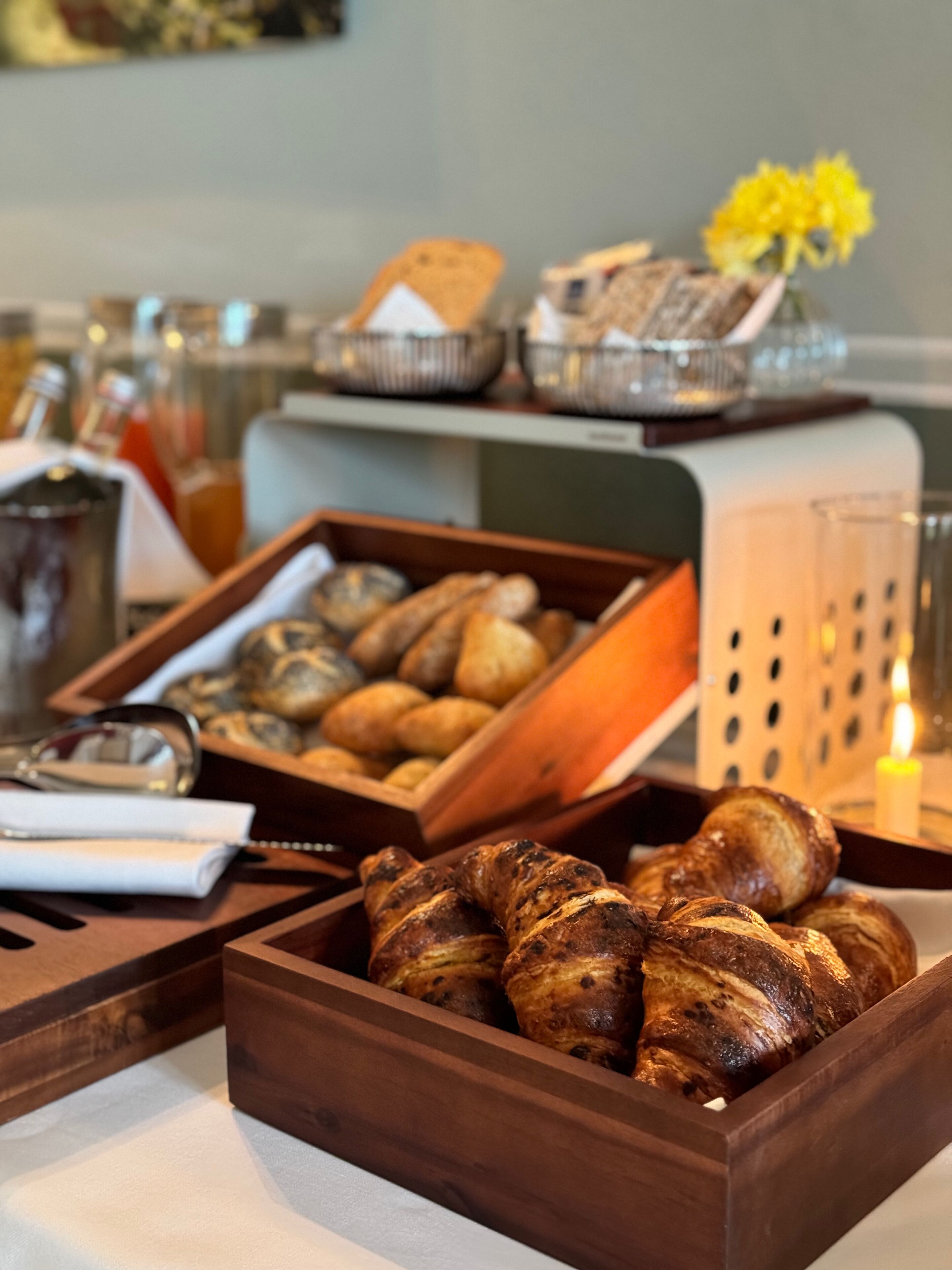 A wooden tray with pastries, a glass of beverage, and a candle on a table.