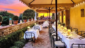 Un área de comedor al aire libre con mesas dispuestas para una comida, rodeada de muros de piedra y plantas en macetas.