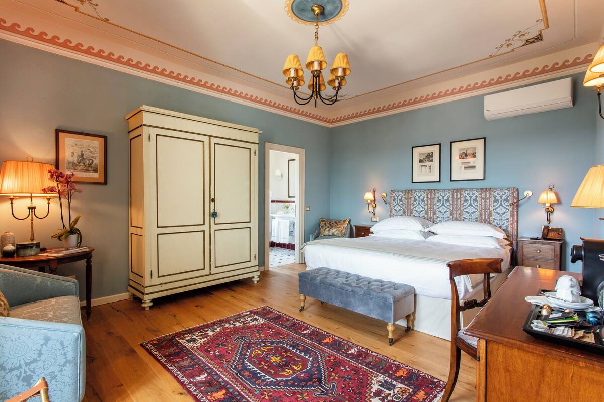 A bedroom with a bed, a desk, a chair, a wardrobe, and a rug.