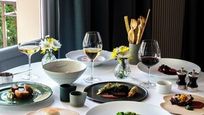 Una mesa de comedor dispuesta con diferentes platos, copas de vino y un jarrón con flores.