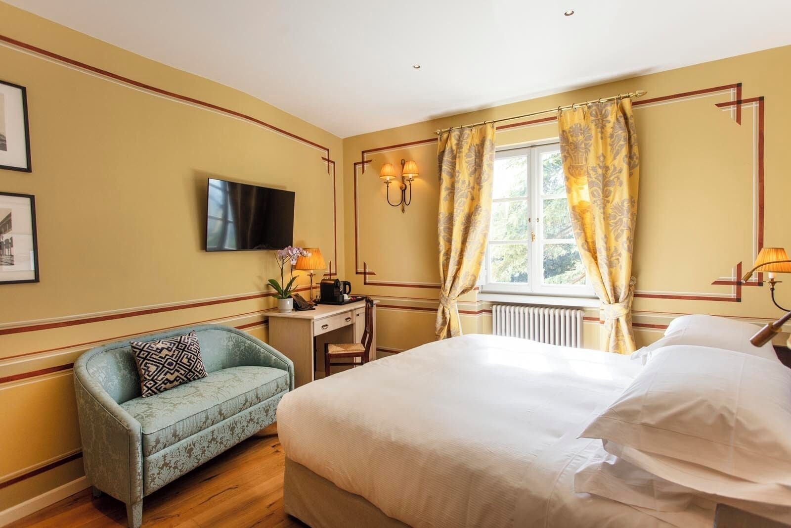 Une chambre d’hôtel équipée d’un lit, d’un bureau, d’une chaise, d’une télévision et d’une fenêtre avec des rideaux.