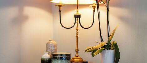 Une table ronde en bois, sur laquelle se trouvent une lampe en laiton, une orchidée en pot, un petit vase et un tableau encadré accroché au mur.