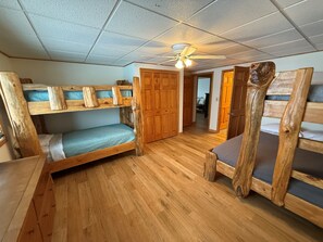 Une chambre avec des lits superposés en bois, un ventilateur de plafond et des portes en bois.
