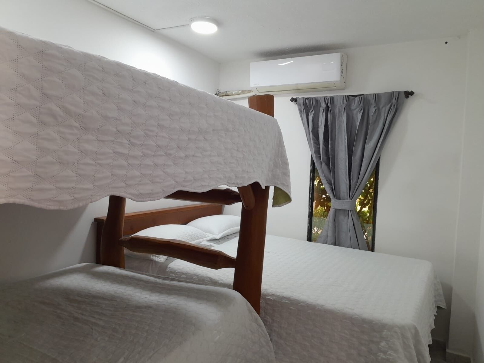 Een slaapkamer met een stapelbed, een houten hoofdbord, wit beddengoed en een airconditioner aan de muur.