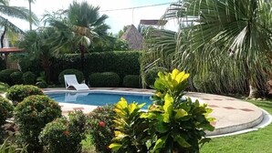 Una piscina rodeada de setos cuidados y palmeras.