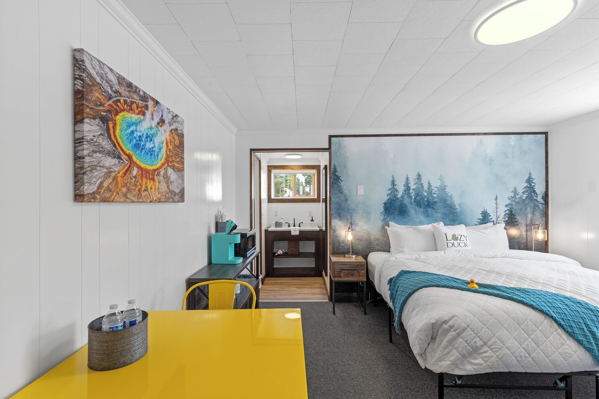 Hotellihuone, jossa on sänky, työpöytä, tuoli, kylpyhuone ja taulu seinällä.