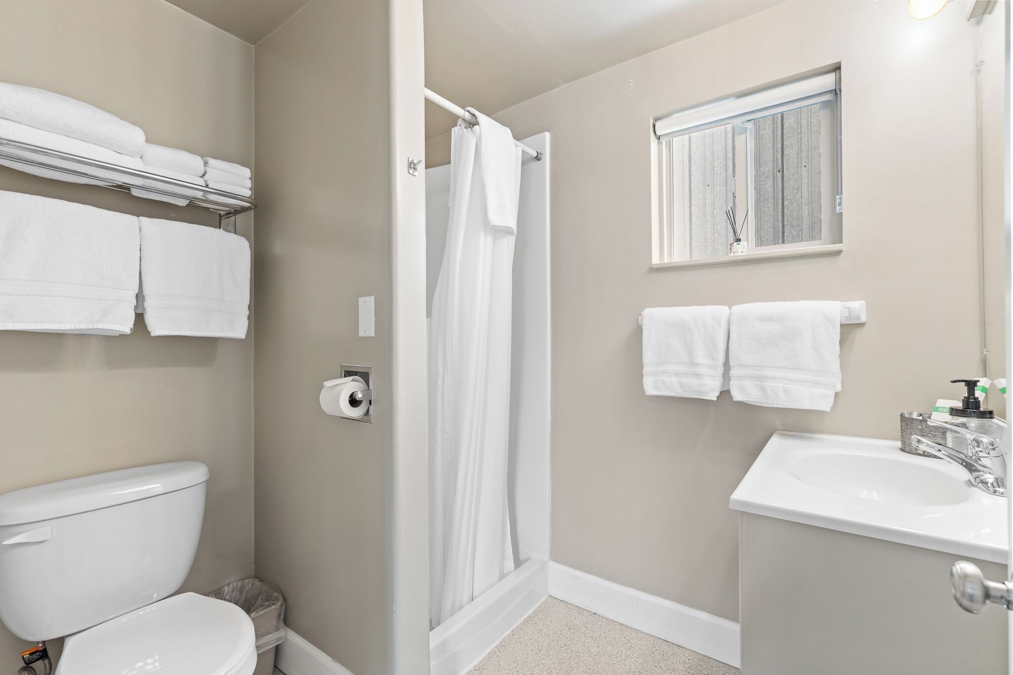 A bathroom with a toilet, a shower, a sink, and towels on a rack.