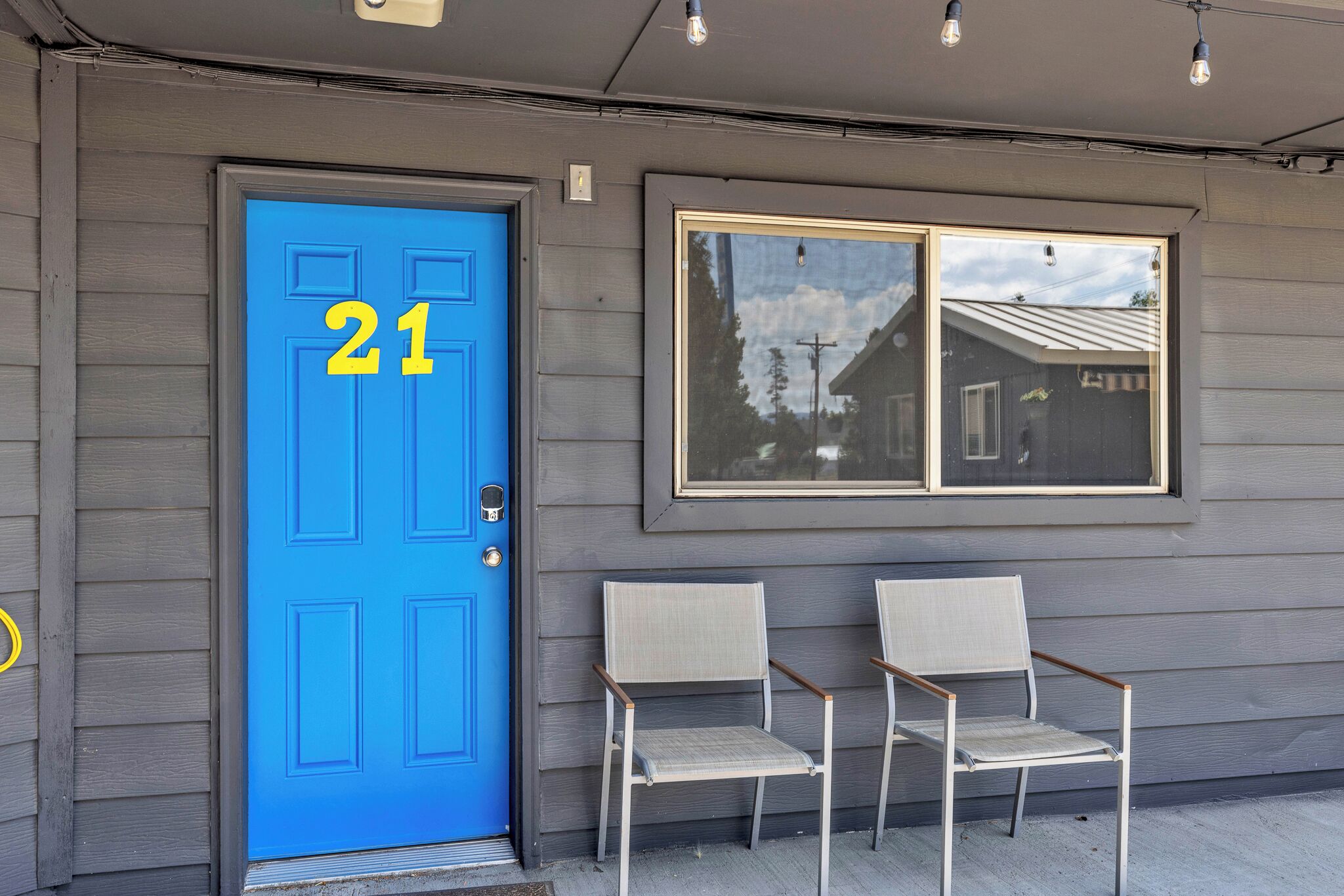 A blue door with the number 21, two chairs outside, and a window reflecting a house.