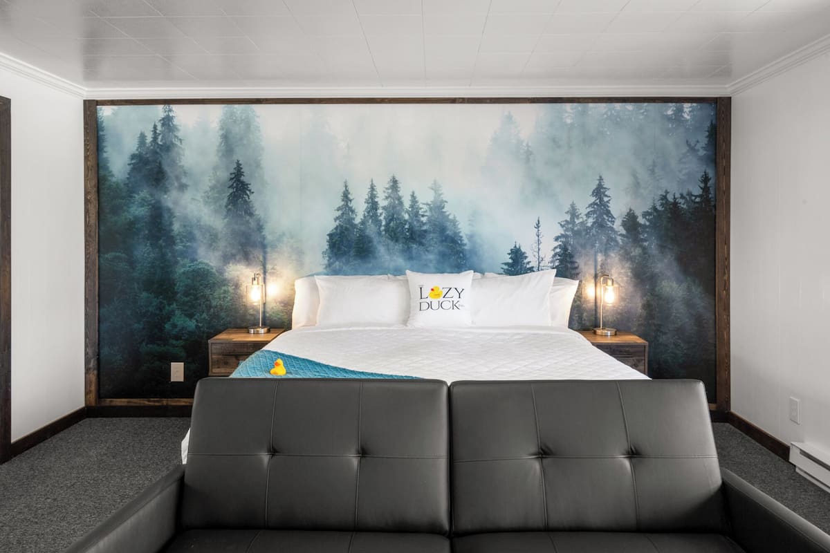 Une chambre à coucher avec une grande fresque représentant une forêt, une tête de lit capitonnée, deux lampes de chevet et un lit moelleux.