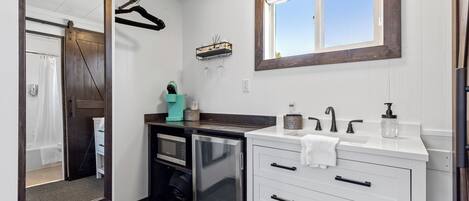 Un baño moderno con un espejo grande, un horno microondas integrado, un lavabo con grifo y una ventana sobre el lavabo.