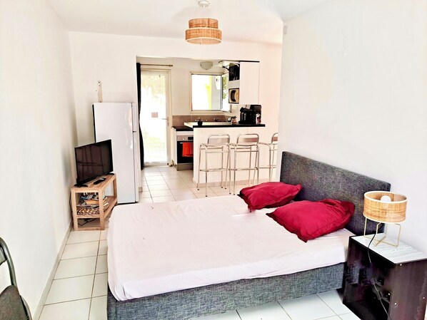 Ein Schlafzimmer mit Bett, Fernseher, Schreibtisch und einer Küchenzeile.