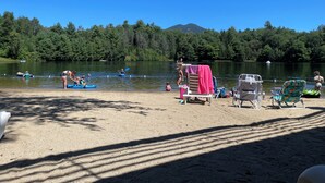Un entorno junto al lago con kayaks, una playa de arena y un fondo arbolado.