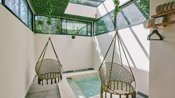 A modern interior with two hanging chairs, a small pool, and a view of greenery through large windows. - Cozy Jungle Retreat, Private Indoor Pool, Breakfast, 5 mins to the Beach (San Miguel de Cozumel)