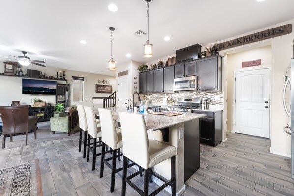 A modern kitchen with a central island, dark cabinetry, and a dining area with chairs.