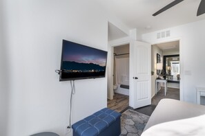 Moderni hotellihuone, jossa on seinälle asennettu taulutelevisio, sininen penkki ja näkymä kaupungin siluettiin auringonlaskun aikaan.