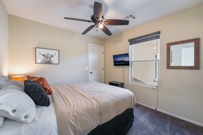 Un dormitorio con una cama, ventilador de techo, televisor, ventana y puerta.