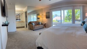 Ein geräumiges Schlafzimmer mit einem großen Bett, einem Nachttisch und Blick ins Freie durch große Fenster.