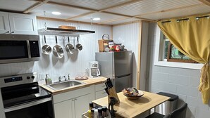 A compact kitchen with a microwave, stove, sink, and hanging pots. There's a small dining area with a table and chairs. - New Guest suite located in Jasper with a mountian view and fire pit (Jasper)