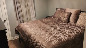 A bedroom with a bed, a nightstand, a dresser, a patterned bedspread, and a ceiling light.