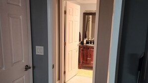 A hallway with wooden flooring leading to a room with a wooden cabinet and a mirror.