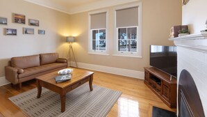 A living room with a brown leather sofa, a wooden coffee table, a TV on a wooden stand, and a fireplace. - Reflections Norah Head Lighthouse Cottages (Norah Head)