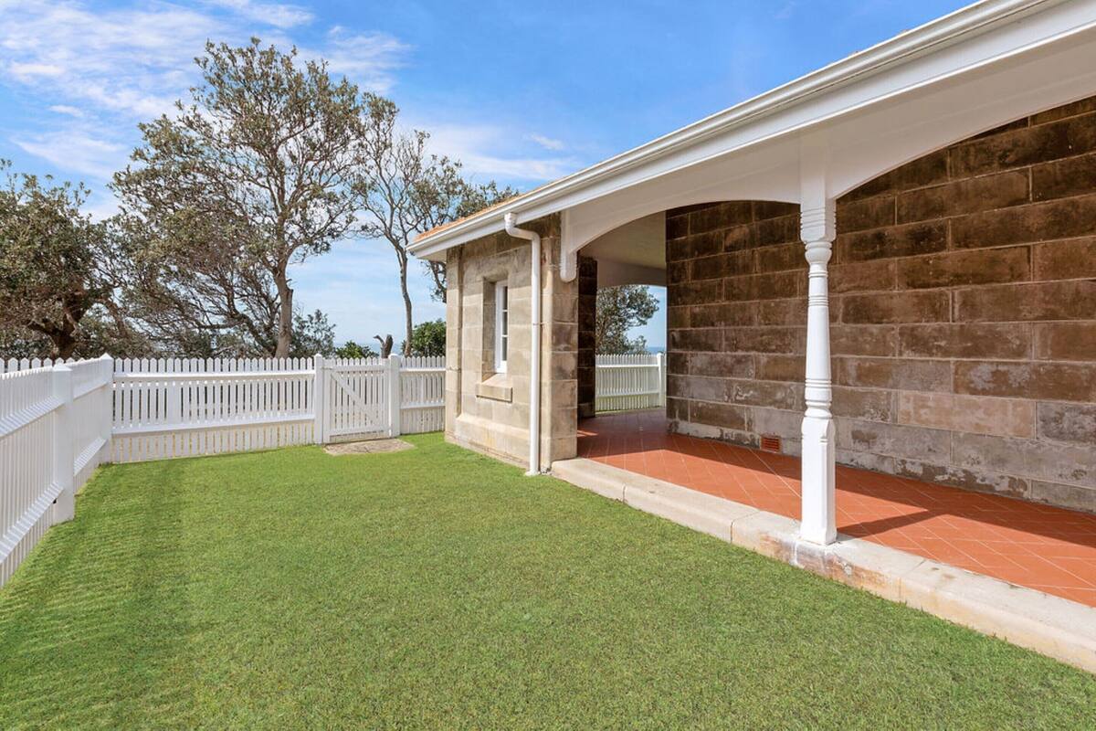 A covered patio area with stone walls and a white fence.