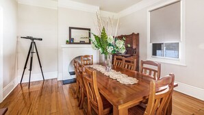 A dining area with a wooden table, chairs, a vase with flowers, a telescope, and a window with a blind. - Reflections Norah Head Lighthouse Cottages (Norah Head)