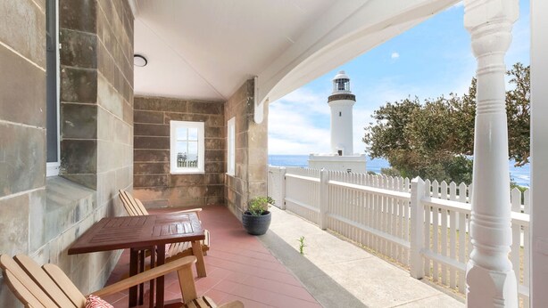 A covered patio with a table and chairs, a potted plant, and a white picket fence. - Reflections Norah Head Lighthouse Cottages (Norah Head)