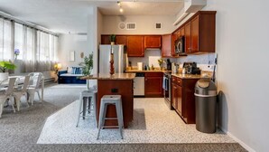 A compact kitchen with wooden cabinets, a stainless steel refrigerator, and a small island with stools. - Sleep 14 | Downtown, Vintage 5bd/2ba (gym+patio) (Chicago)