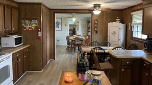 A kitchen with wooden cabinets, a microwave, a stove, a dining table with chairs, and a ceiling fan.