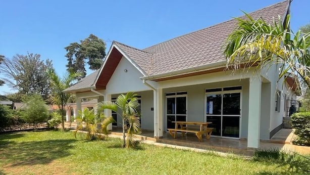 A two-story house with a covered patio, a lawn, and a small garden with palm trees. - Sega Lodge (Sega)