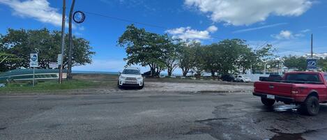 Ein Parkplatz mit einem weißen Auto und einem roten Pickup, ein Schild mit der Aufschrift 'D's Landing Brunch' und im Hintergrund der Blick aufs Meer.