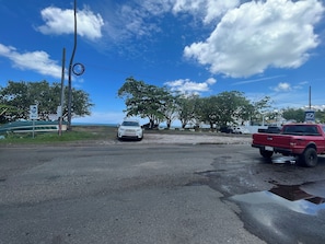 Un espace de stationnement avec une voiture blanche et un camion rouge, un panneau indiquant « D's Landing Brunch », et une vue sur la mer en arrière-plan.
