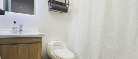 A bathroom with a toilet, a sink with a mirror, a shelf with a decorative item, and a shower curtain.
