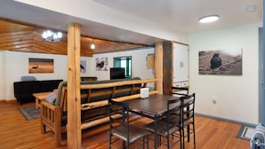 A rustic wooden dining area with benches and a table, a black sofa, and a television in the background.