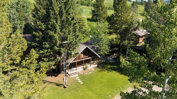 A wooden cabin surrounded by dense forest, with a clear view of the surrounding hills.
