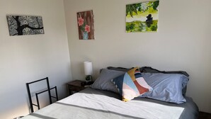 Un letto rifatto con cura, un cuscino decorativo colorato, un comodino con una lampada e due quadri alle pareti.