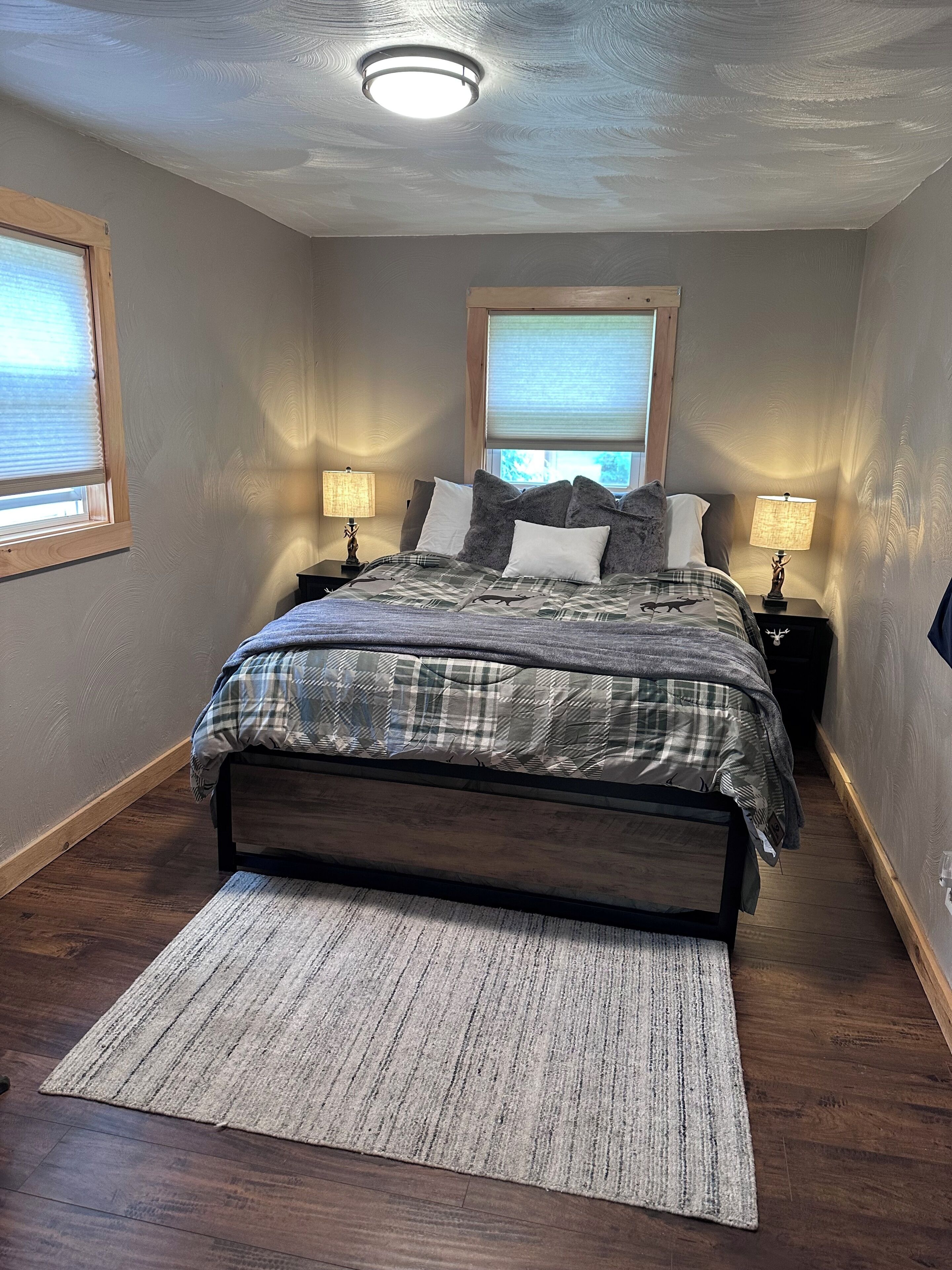 A bedroom with a large bed, two bedside tables with lamps, a window, and a wooden floor.