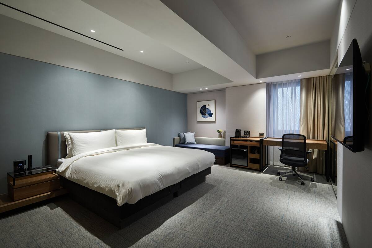 Une chambre d’hôtel moderne, dotée d’un grand lit, d’un bureau et d’une télévision.
