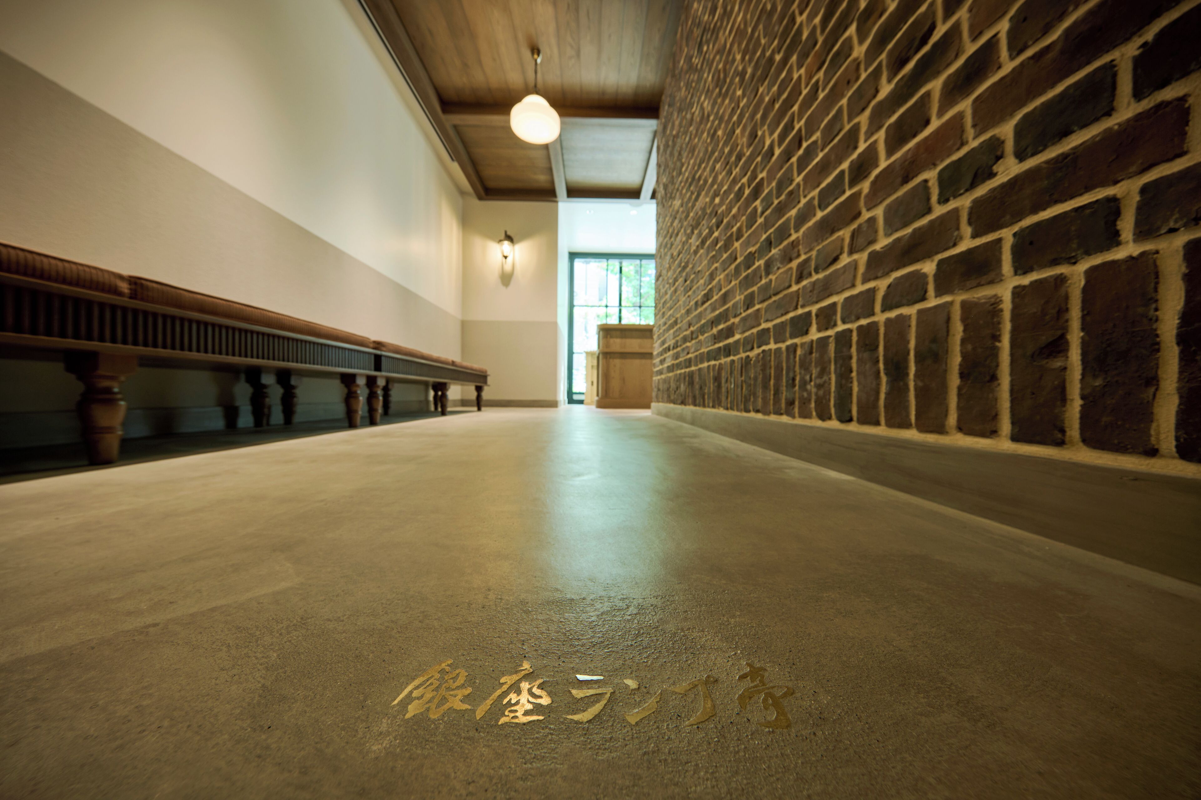 A spacious interior with a high ceiling, a brick wall, and a row of benches along one side.