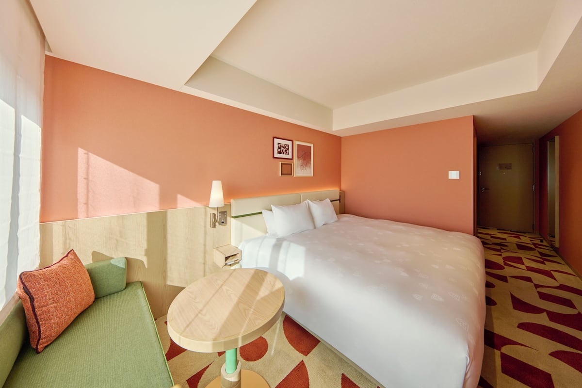 A hotel room with a large bed, a small sofa, a round table, and a nightstand.