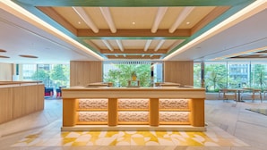 A modern hotel lobby with a central reception desk, large windows, and a view of greenery outside. - The Royal Park Hotel Ginza 6-chome (Tokyo)