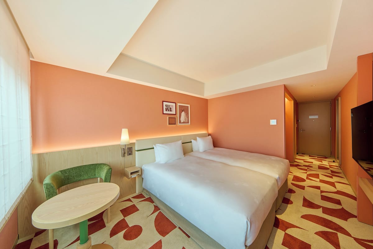 A hotel room with a large bed, a small round table, a green chair, and a TV.