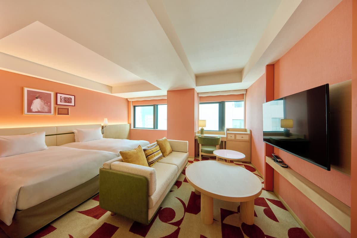 A hotel room with two beds, a sofa, a dining table, a TV, and a window.
